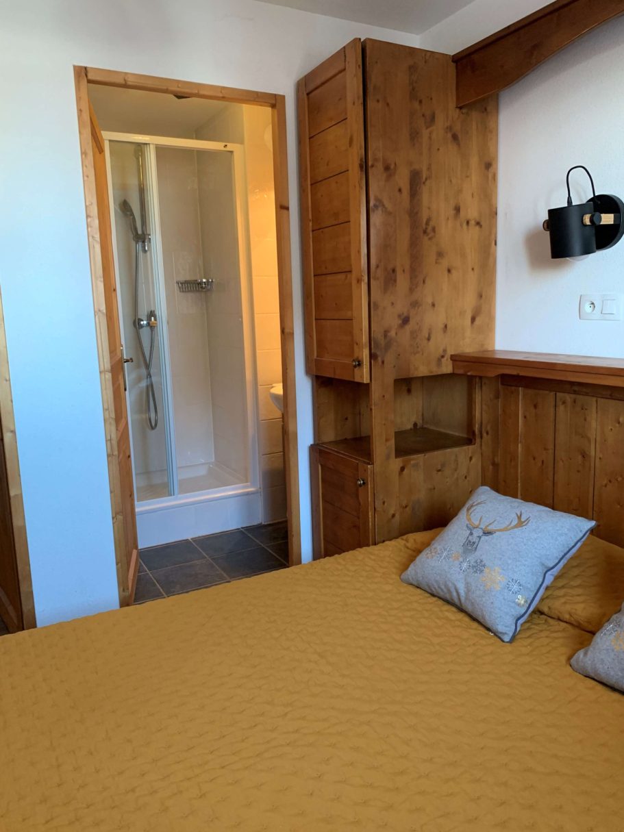 Chambre avec lit, mur en bois, et une salle de bain attenante visible.