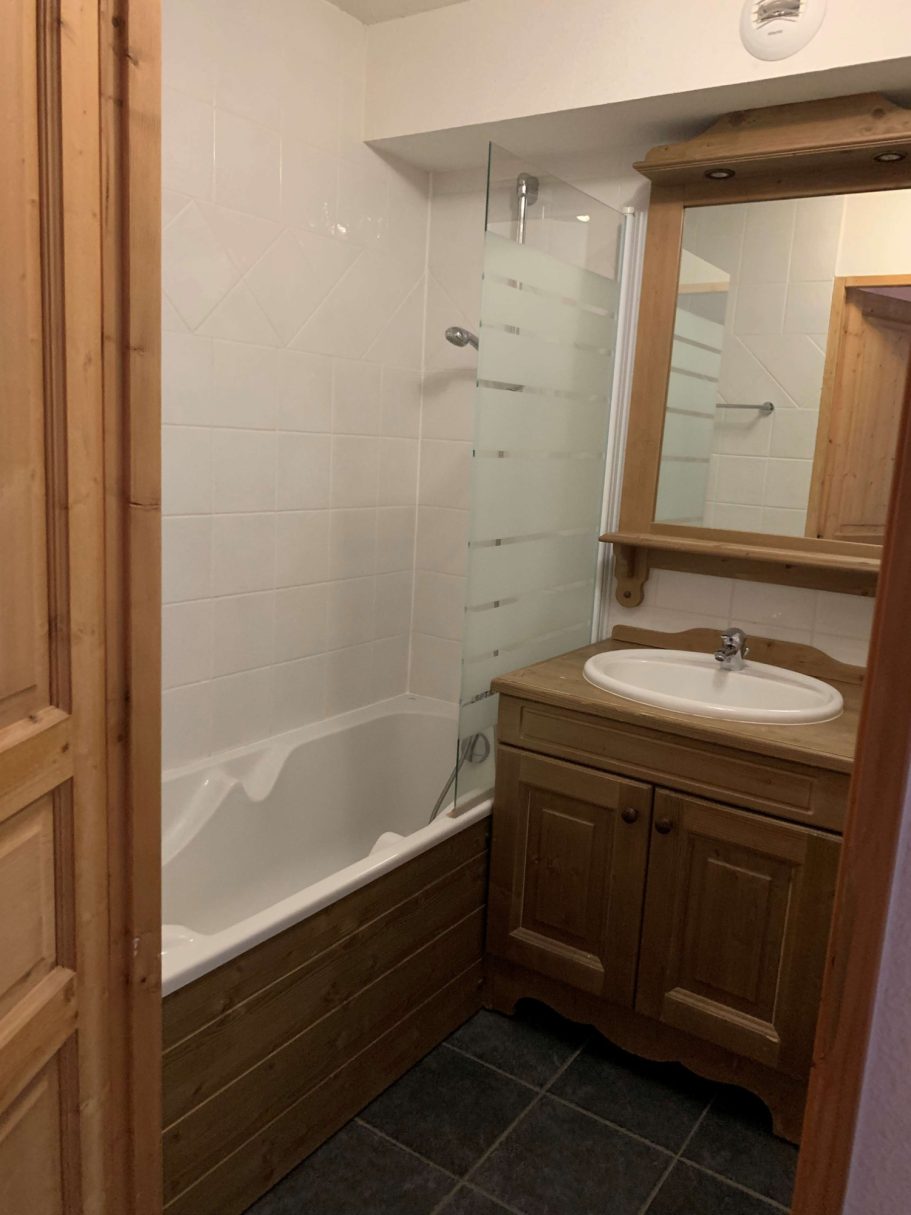 Salle de bains moderne avec baignoire, lavabo en bois et miroir. Moquette grise.