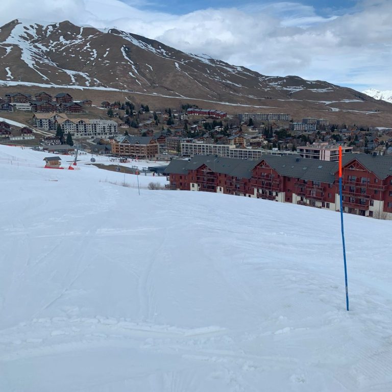 Pente de ski avec des bâtiments en bois et des montagnes en arrière-plan.