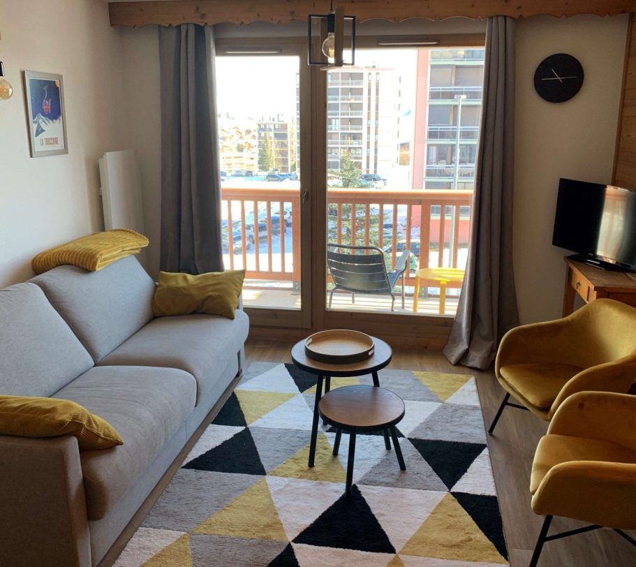 Salon moderne avec un canapé gris, des chaises jaunes et une vue sur le balcon.