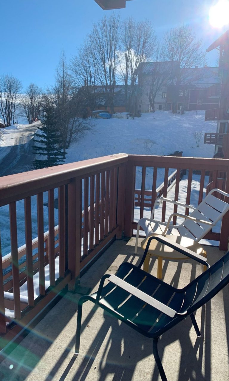 Balcon avec chaises surplombant une neige immaculée et le soleil brillant.