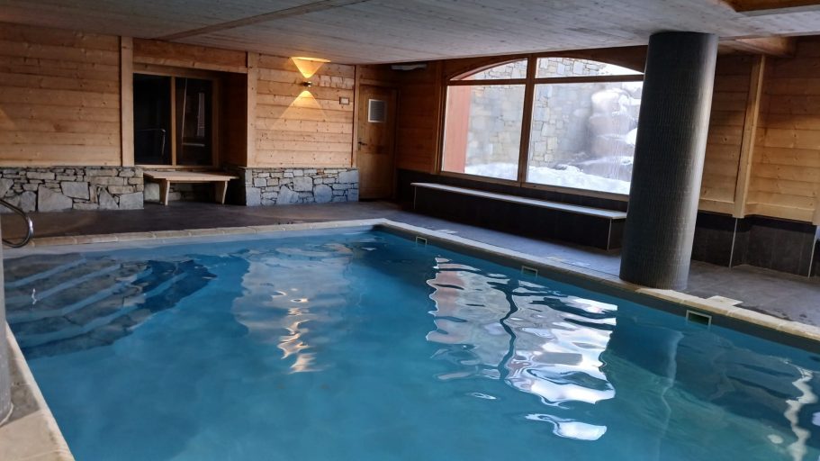 Piscine intérieure avec murs en bois et grandes fenêtres éclairant l'espace.